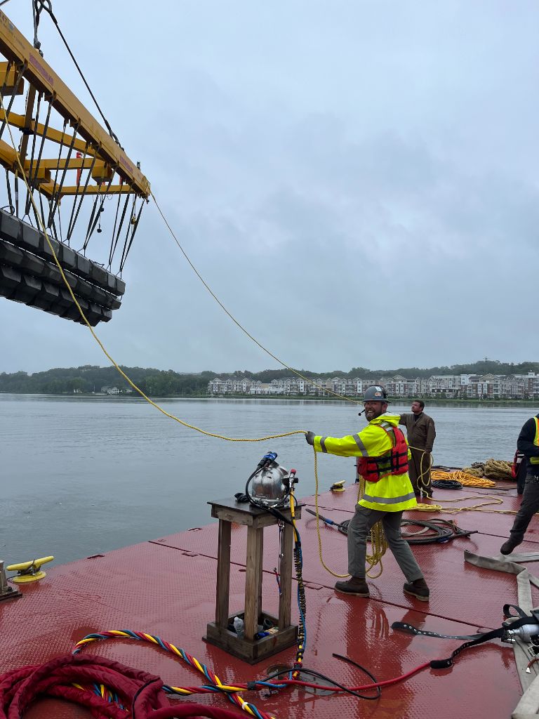 SubCon crew working on a barge during a marine construction operation — safety vessel rigging and crane operations on the water