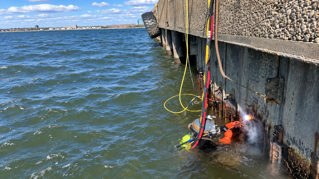Commercial diver in orange gear working at bridge pier waterline — SubCon Submerged Construction